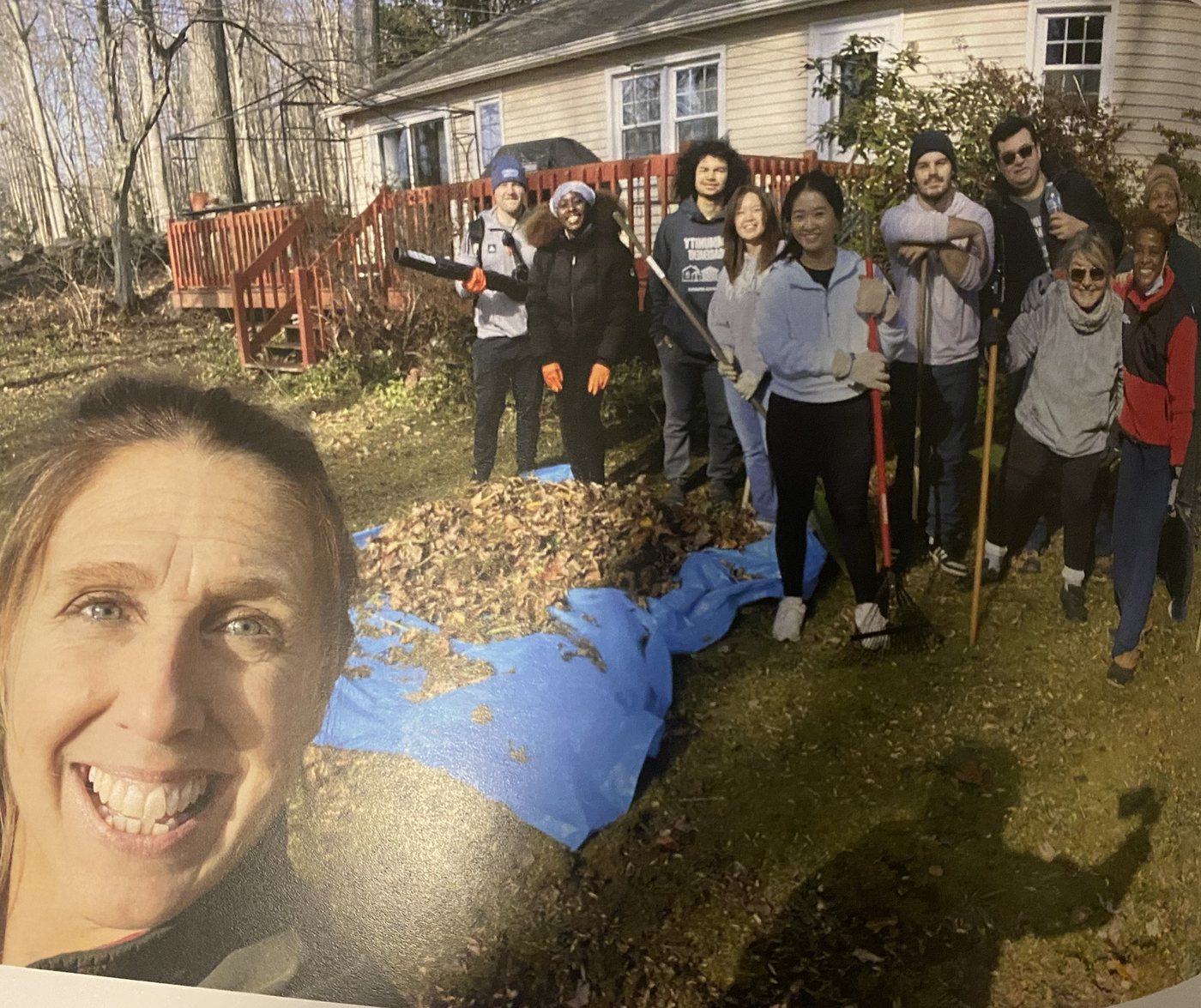 A group of volunteers with rakes beside a pile of leaves in a yard